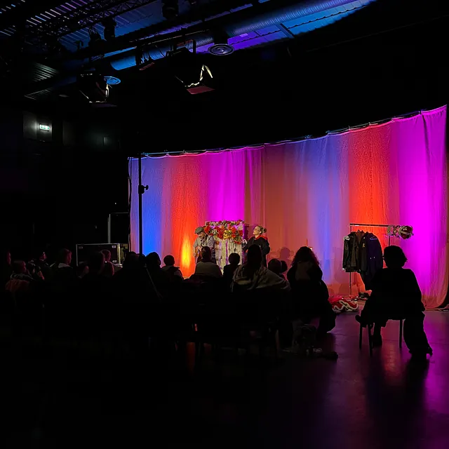 Teaterforestilling med fargerik lyssetting, publikum følger skuespill på scenen.