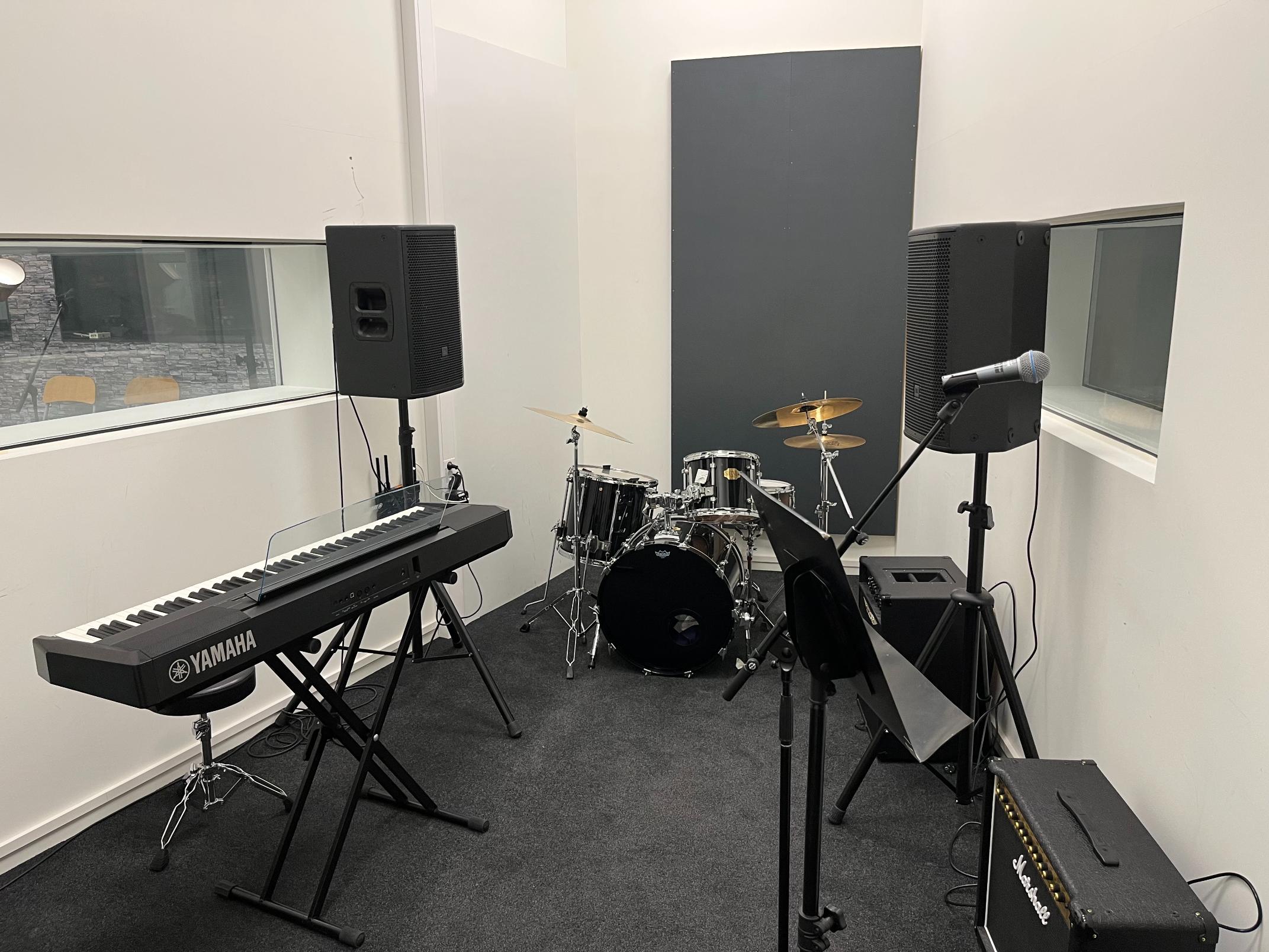 Øvingsrom med trommesett, elpiano, mikrofon og høyttalere klart for bandprøve.
