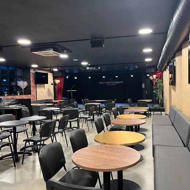 Kaféområde med runde bord, svarte stoler og liten scene på Kulturfabrikken Kristiansund.