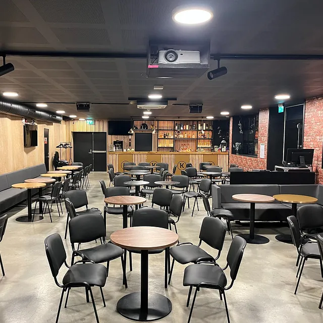 Moderne bar og sitteområde med svarte stoler og trebord, klar for arrangement.